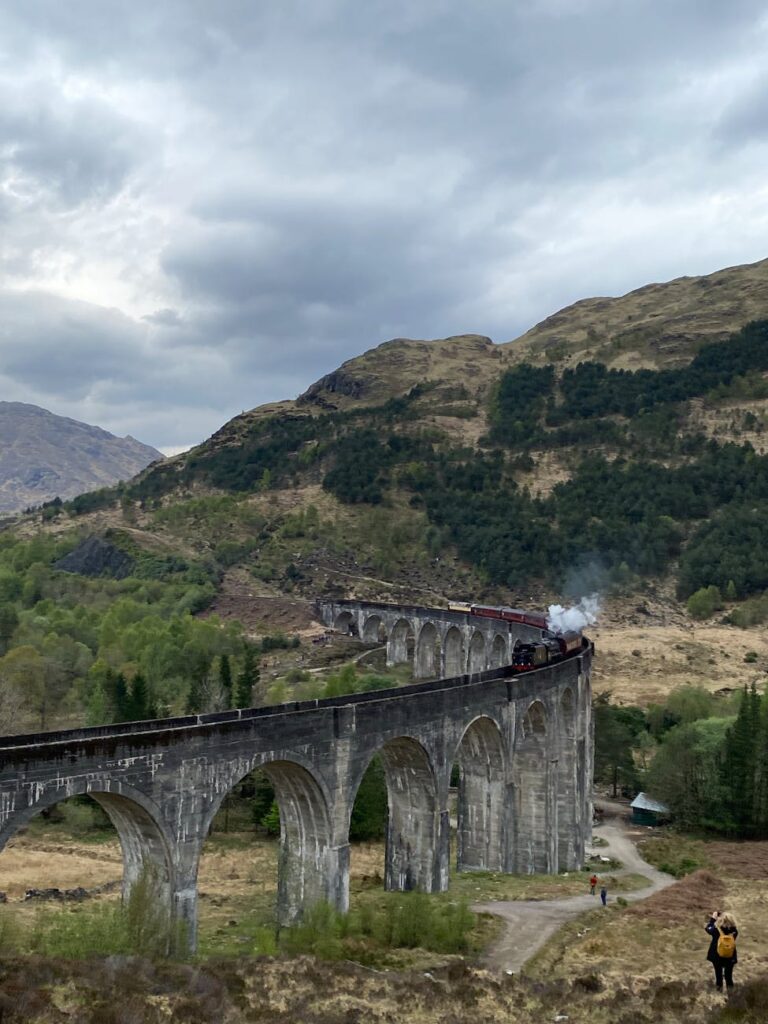 steam train crossing glenfinnan viaduct in scotland