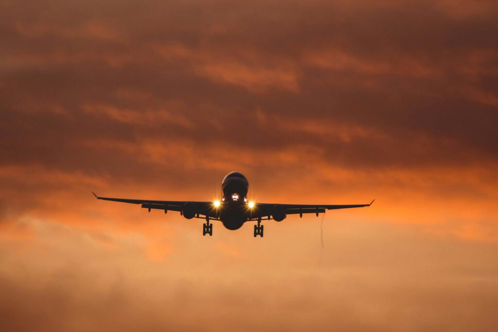 airplane flying under orange sky at sunset